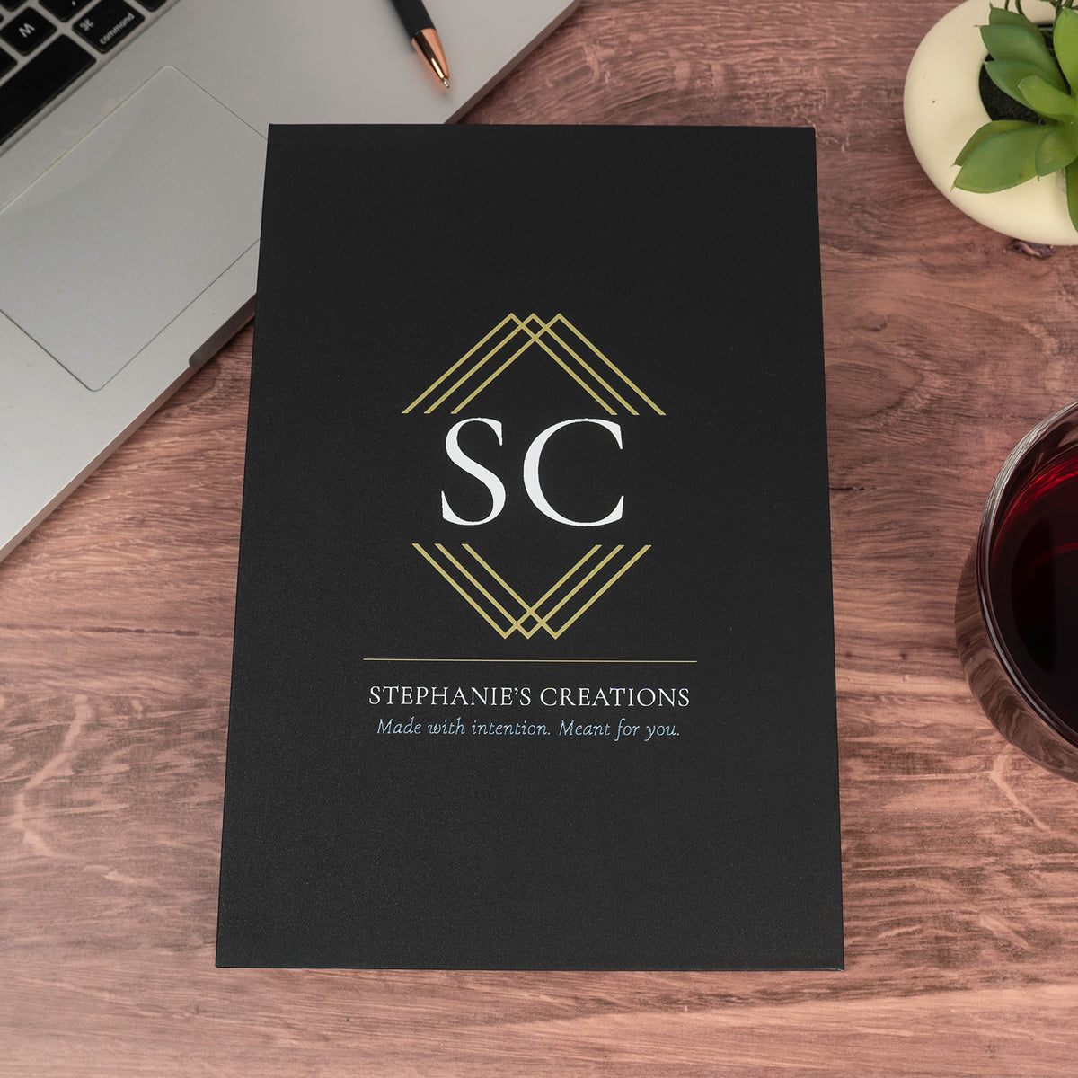 Black Stephanie's Creations gift box featuring a gold geometric logo and company name on a wooden surface.