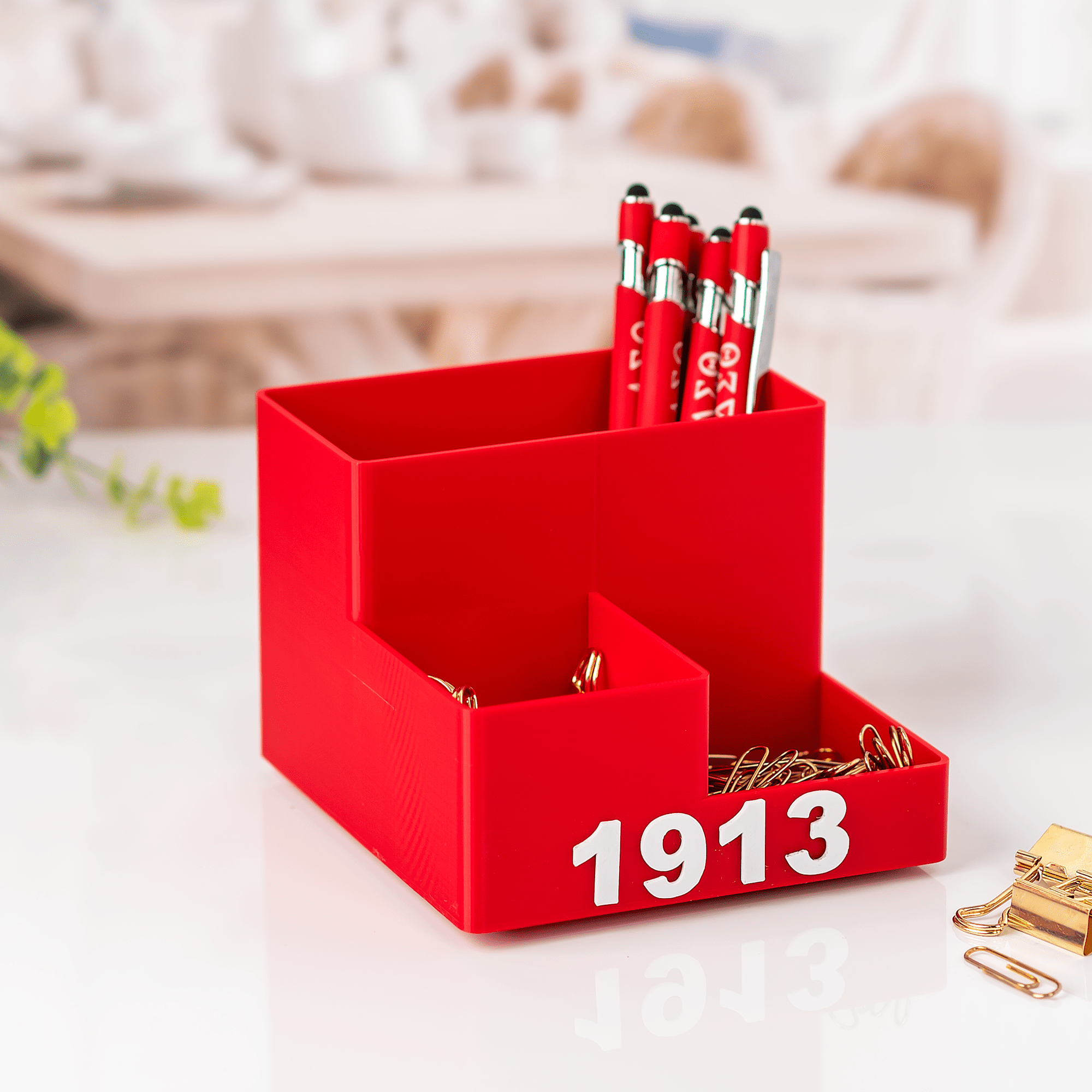 DST 1913 crimson desk organizer filled with Greek letter pens and gold paper clips on bright desk