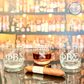 Phi Beta Sigma whiskey glasses displayed on a reflective surface, engraved with the fraternity’s Greek letters, featuring an elegant bar background, officially licensed Phi Beta Sigma product, glass filled with whiskey, sleek and professional design, perfect fraternity gift, set of engraved whiskey glasses, ideal for special occasions and celebrations, includes cigar for added sophistication, unique barware for fraternity members and alumni.